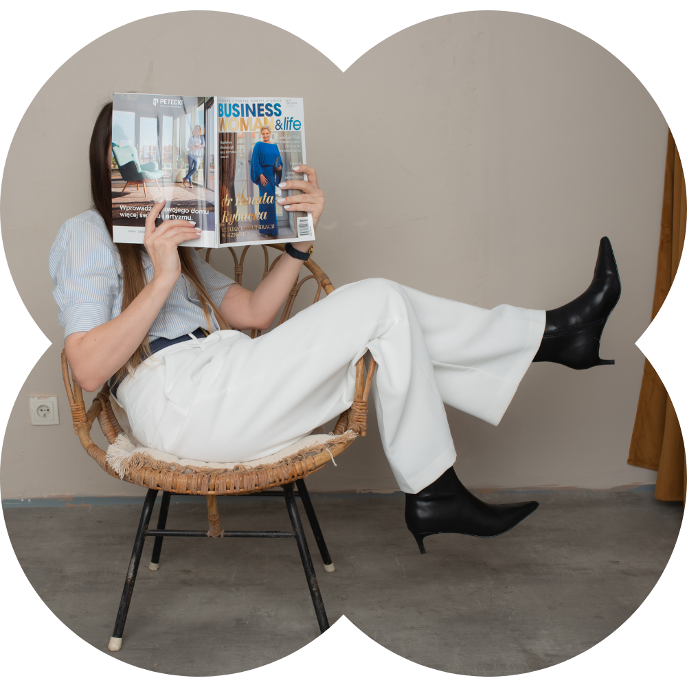 Stylowe zdjęcie kobiety w białych spodniach i czarnych botkach, siedzącej bokiem na krześle i czytającej magazyn – kreatywny, humorystyczny portret Patie Projektuje, oddający jej styl i podejście do projektowania.